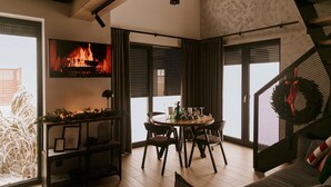 A cozy living room with a fireplace, a dining area with a round table and chairs, and a staircase with a wreath. - Holiday Home, Bedroom With Bathtub, Jacuzzi (Koscierzyna)