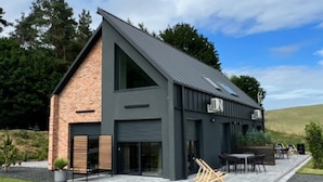 A modern house with a sloped roof, large windows, and a patio area with outdoor furniture. - Holiday Home, Bedroom With Bathtub, Jacuzzi (Koscierzyna)