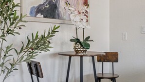 Una habitación con una mesa redonda, dos sillas, una planta en maceta y un cuadro en la pared.