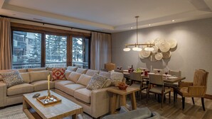 Una sala moderna con un sofá grande, una mesa de comedor y sillas. Hay ventanas grandes con cortinas, un candelabro y un adorno de plato en la pared.