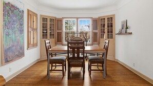 A dining area with a wooden table and chairs, large windows, and a painting on the wall. - MINNeSTAY* Como Classic (St. Paul)