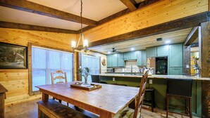 Un interior de madera con una mesa de comedor, sillas, una zona de cocina con armarios verdes y una lámpara colgante.