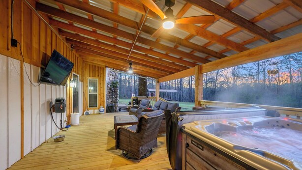 Un espacio al aire libre techado con un jacuzzi, muebles de mimbre y un televisor montado en la pared.