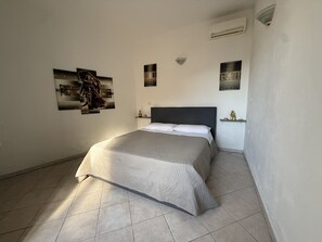 A bedroom with a bed, wall-mounted artwork, a nightlight, and a ceiling fan. - Essenedda Holiday Home: Two-Room Apartment in the Historic Center (Orosei)