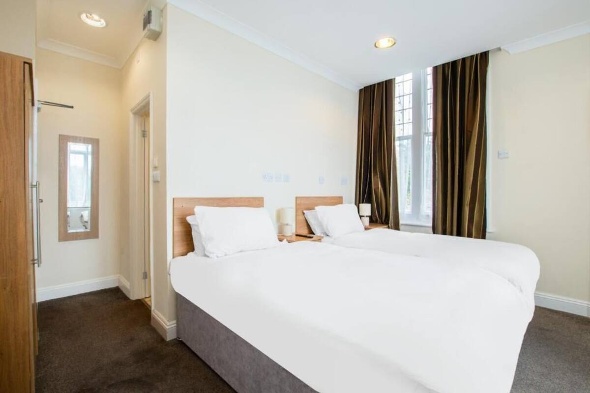 Une chambre d’hôtel avec un grand lit, deux tables de chevet, un miroir et une fenêtre avec des rideaux.