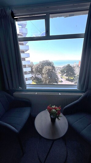 A room with a large window, two sofas, a small table with a flower vase, and a radiator.
