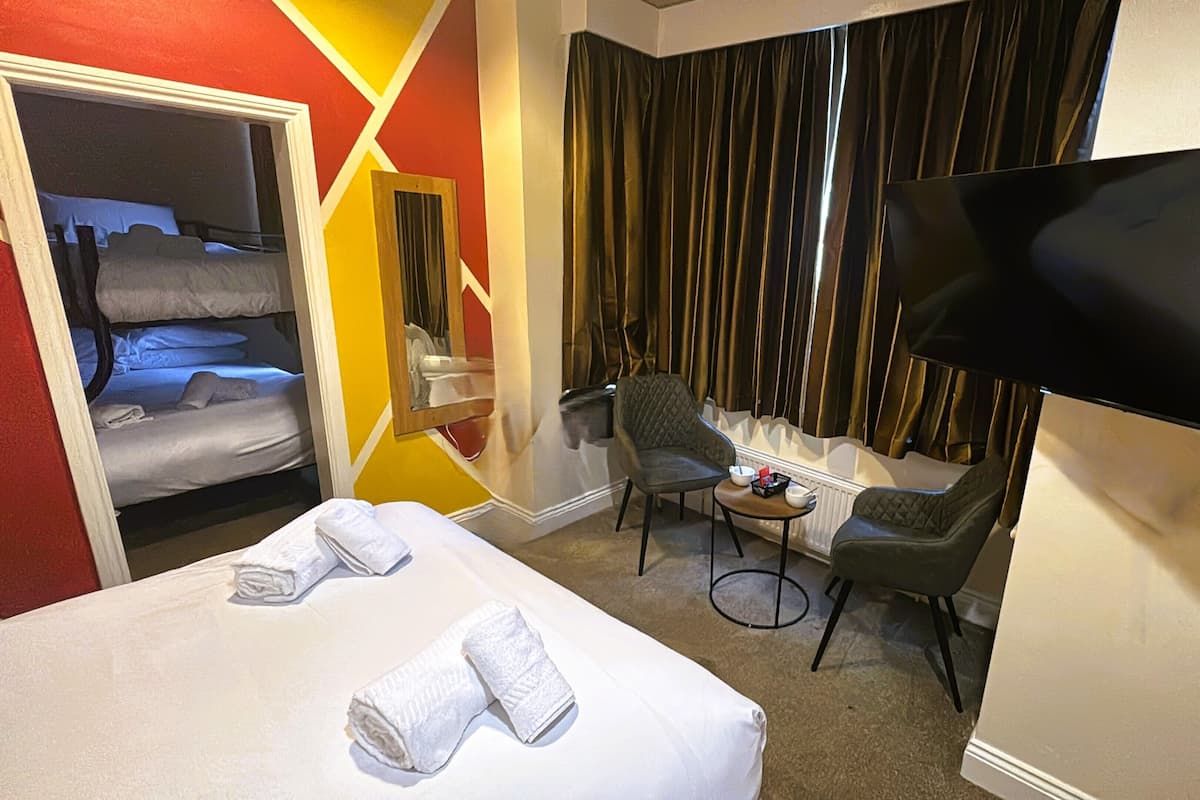 Une chambre d’hôtel avec un lit, une chaise, une petite table, un téléviseur et une fenêtre avec des rideaux.