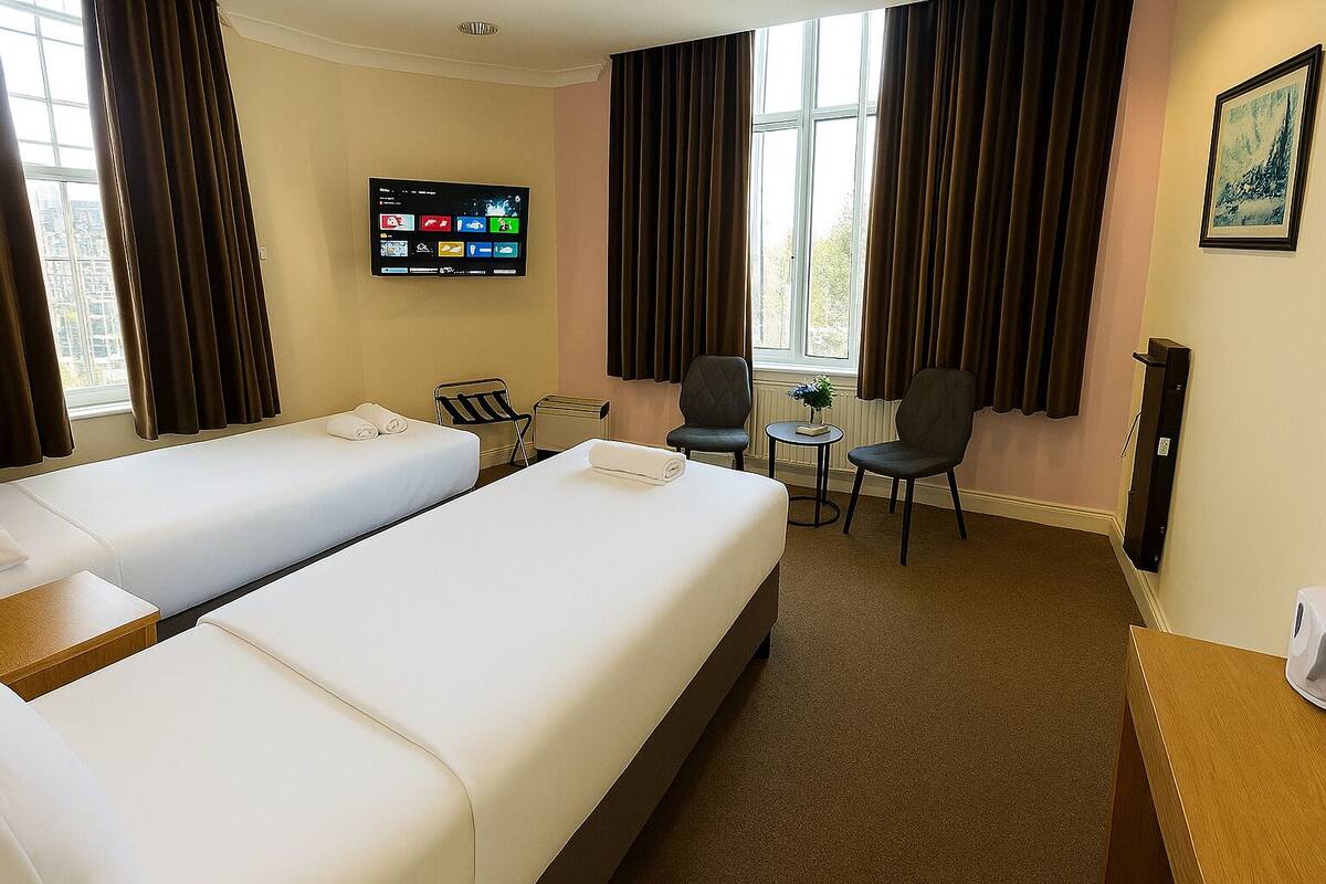 Une chambre d’hôtel avec deux lits, une télévision, une petite table avec des chaises et une fenêtre avec des rideaux.