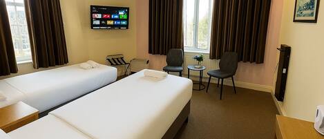 Habitación de hotel con dos camas, televisión, una pequeña mesa con sillas y ventana con cortinas.
