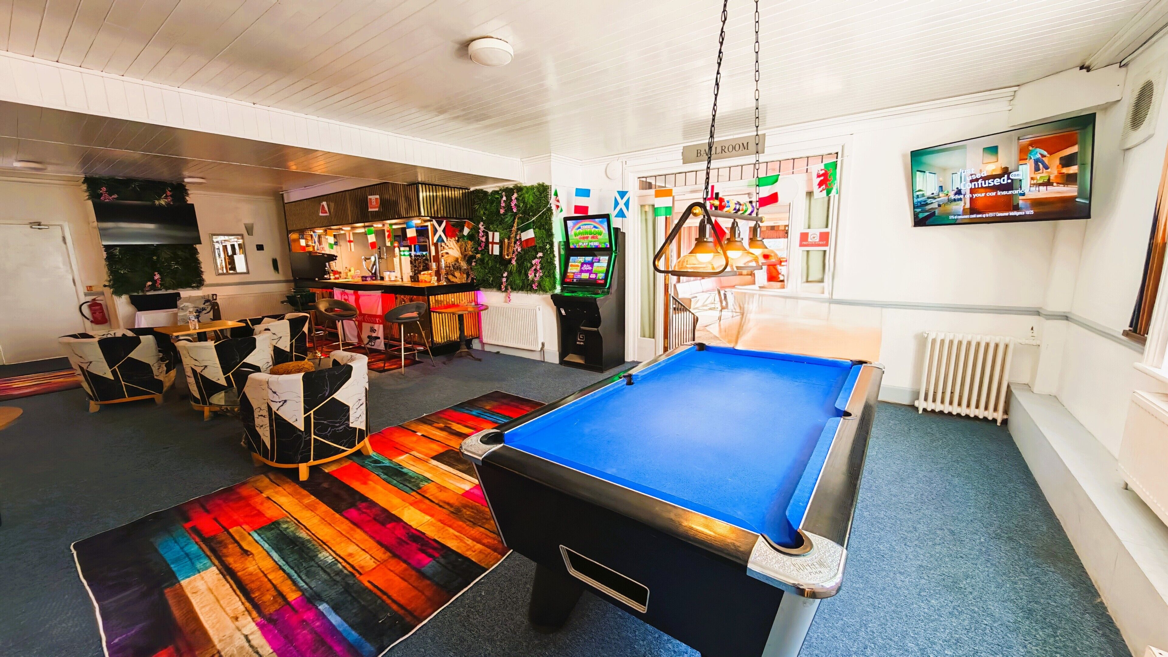A pool table, bar area, and seating in a room with white walls and a ceiling fan.