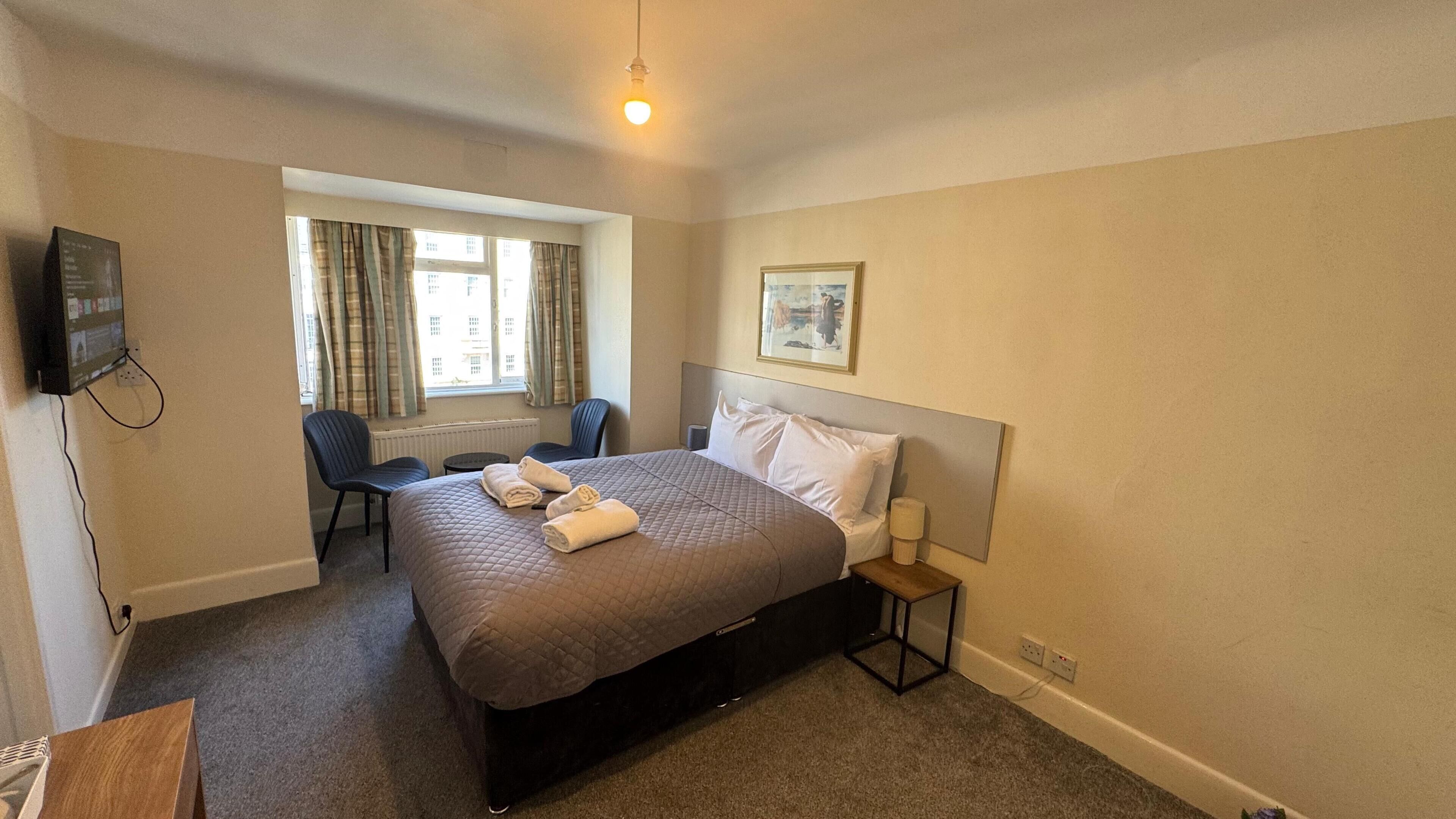 A hotel room with a bed, a desk, a chair, a television, and a window with curtains.