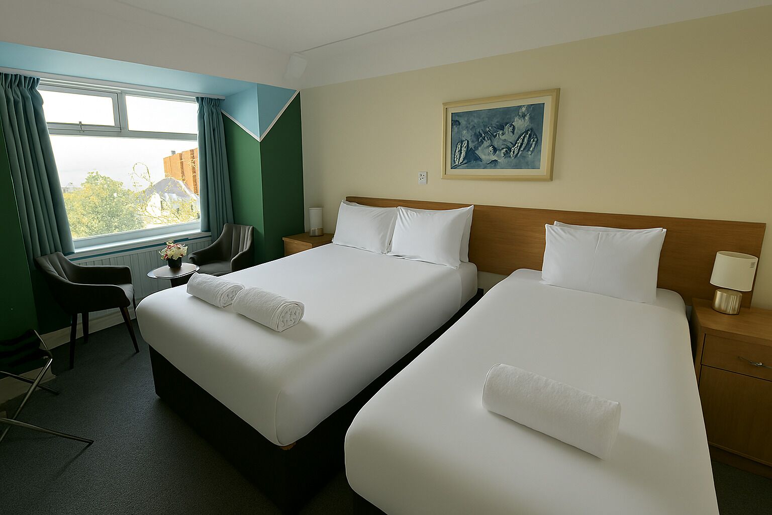 A hotel room with two beds, a desk, a chair, a window with curtains, and a painting on the wall.
