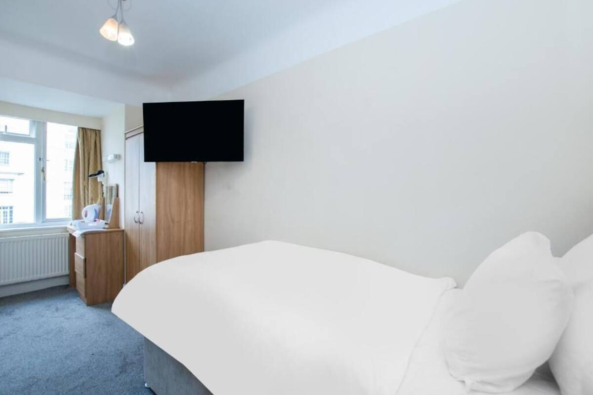 Une chambre d’hôtel avec un lit, un bureau, un téléviseur fixé au mur et une fenêtre avec des rideaux.