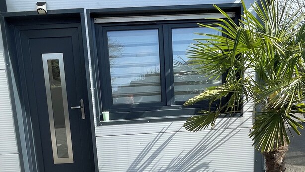 Un edificio moderno con una puerta oscura, ventanas grandes y una planta en maceta.