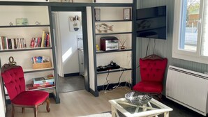 Una sala de estar con un sofá, una silla roja, una mesa de centro, una estantería y un televisor.