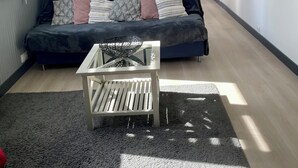 Un salón moderno con un sofá azul oscuro, una mesa de centro de vidrio y un ventanal con persianas.
