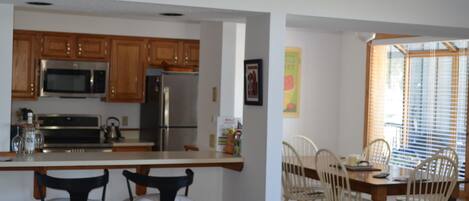 A kitchen with wooden cabinets, a microwave, and a refrigerator. There is a dining area with a table and chairs.