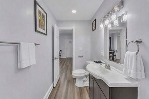 Un baño moderno con inodoro blanco, tocador y un espejo grande con luces.