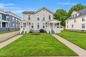A two-story residential building with a front porch, a covered outdoor seating area, and a well-maintained lawn.