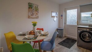 A dining area with a round table, colorful chairs, a vase with flowers, and a washing machine in the corner. - Ash House 3 Bedroom in Cumbernauld (Glasgow)