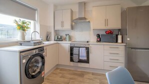 A compact kitchen with a washing machine, oven, microwave, and a refrigerator. - Ash House 3 Bedroom in Cumbernauld (Glasgow)