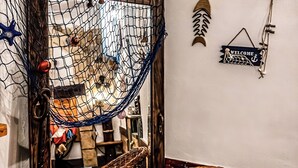 En fletstol med pude, en hængekøje og vægdekorationer, herunder en fisk og et velkommenskilt.