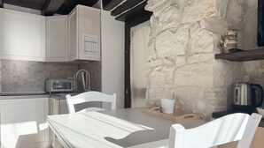 Une cuisine avec des meubles blancs, un mur en pierre, une table en bois et des chaises blanches.