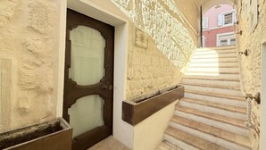 Un escalier étroit doté d’une rampe en bois, une porte avec un panneau en verre dépoli et un mur texturé orné d’un motif décoratif.