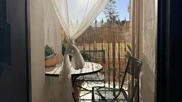 Une terrasse avec une table et des chaises, un pot de fleurs et une clôture en bambou.