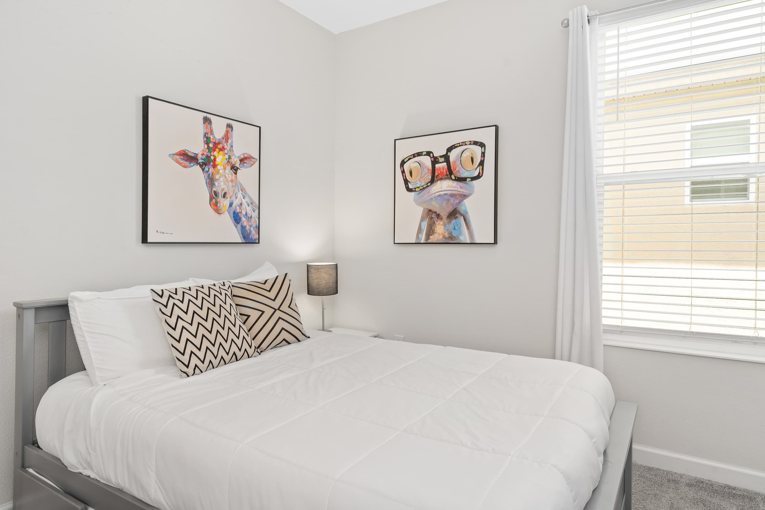 Een slaapkamer met een bed, twee kunstwerken aan de muur, een bedlampje en een raam met zonwering.