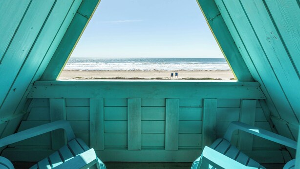 Blick auf einen Strand aus einem Raum mit türkisfarbenen Wänden und Holzbanken.
