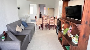 A living room with a grey sofa, a wooden entertainment unit with a TV, and a dining area with a table and chairs. - Relax in paradise (Playa del Carmen)