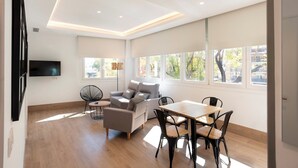 Ein modernes Wohnzimmer mit einer Couch, einem Esstisch und Stühlen, einem flachbildfernseher an der Wand und großen Fenstern mit Ausblick.