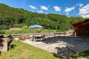 Une terrasse avec une table et des chaises, un parasol bleu et un bâtiment en bois avec un toit rouge.