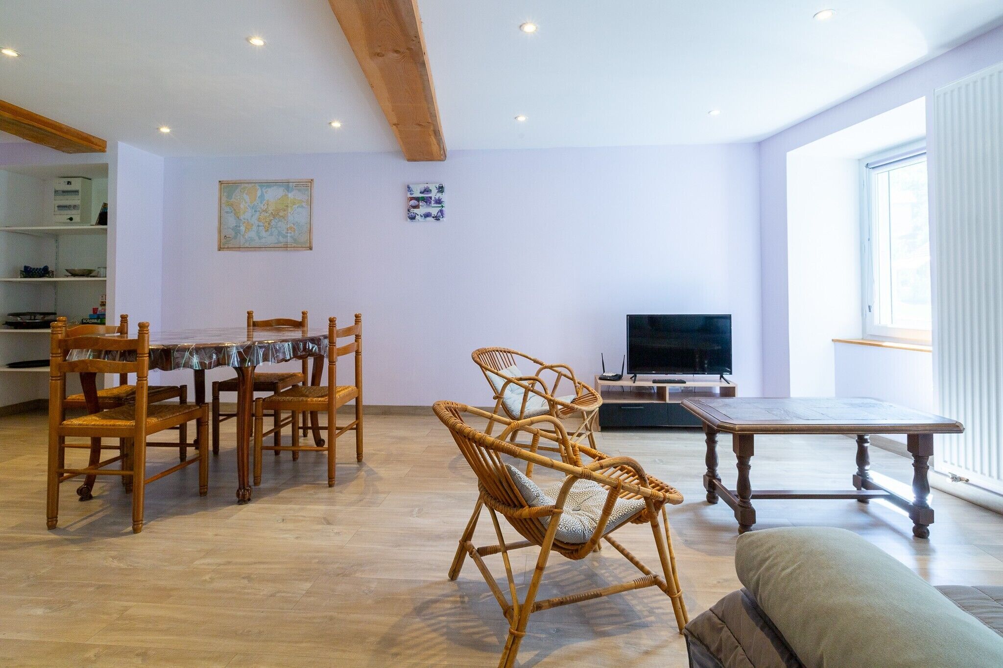 Een woonkamer met een eettafel, rieten stoelen, een bank, een televisie en een kaart aan de muur.