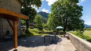 Une terrasse avec une table et des chaises, une pergola en bois et un mur en pierre.