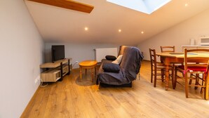 A loft-style room with a skylight, wooden flooring, a sofa, a dining table with chairs, and a TV. - Apartment 'Dans Hameau Du Vercors' with Shared Terrace and Wi-Fi (Saint-Agnan-en-Vercors)