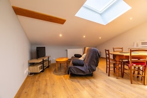 A loft-style room with a skylight, wooden flooring, a sofa, a dining table with chairs, and a TV. - Apartment 'Dans Hameau Du Vercors' with Shared Terrace and Wi-Fi (Saint-Agnan-en-Vercors)