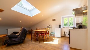 A loft-style room with a skylight, wooden flooring, a dining table with chairs, a sofa, a kitchenette, and a window. - Apartment 'Dans Hameau Du Vercors' with Shared Terrace and Wi-Fi (Saint-Agnan-en-Vercors)