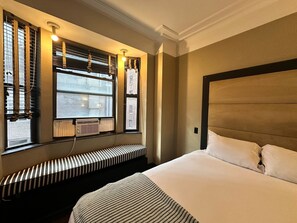 A hotel room with a large bed, a window with blinds, a radiator, and a bench. - Brooklyn Finest Suites (Brooklyn)