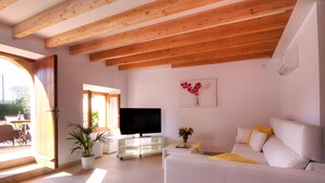 A modern living room with a white sofa, a flat-screen TV, a potted plant, and a painting of flowers on the wall. - Villa 'Can Bandris' with Mountain View, Wi-Fi and Air Conditioning (Illes Balears)