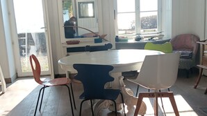 Un comedor con una mesa y sillas blancas, un ventanal y vistas al exterior.