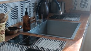 Una cocina con salpicadero de baldosas a cuadros, encimera de madera, un lavabo y una tetera.
