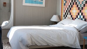 Una habitación de hotel con una cama, un espejo, un cuadro, un tapiz estampado y una pared a cuadros.