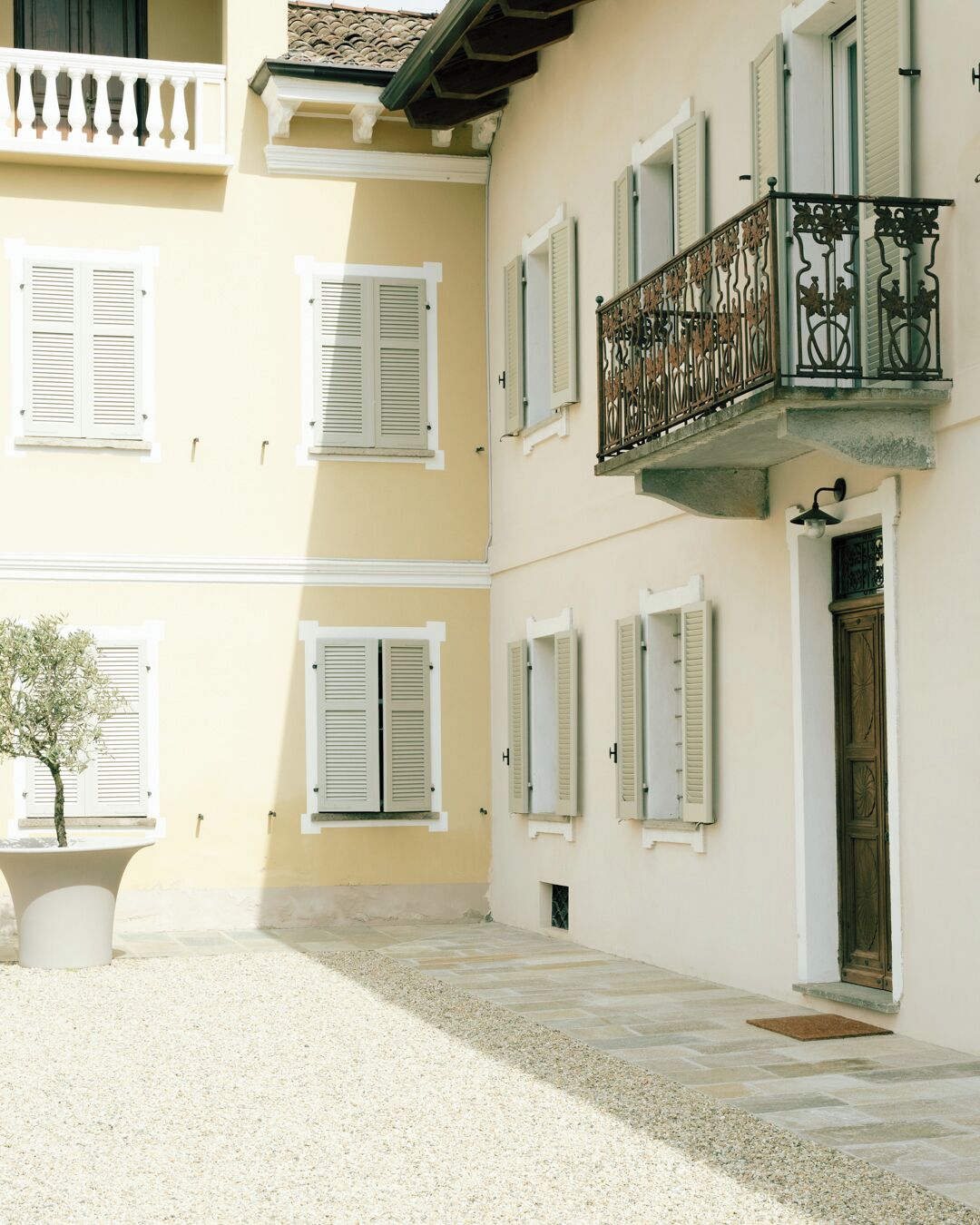 A building with multiple windows, a balcony with ornate metal railings, and a small tree in a planter.