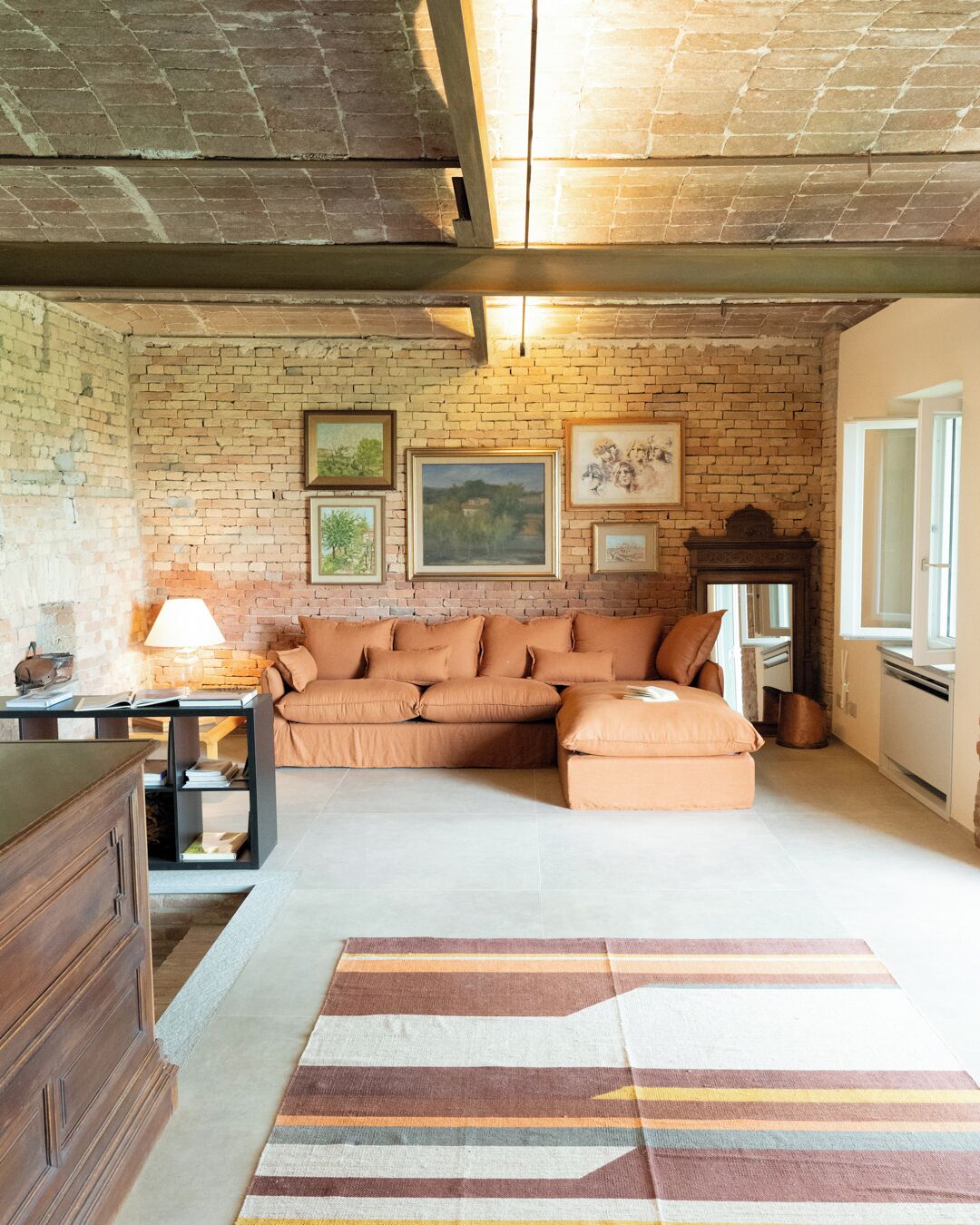 A cozy living room with a brick wall, a sectional sofa, a wooden cabinet, and a patterned rug.