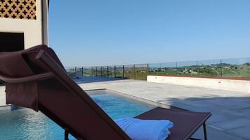 Une chaise longue installée au bord de la piscine, avec une serviette à portée de main, offrant une vue dégagée sur la piscine et un paysage lointain.