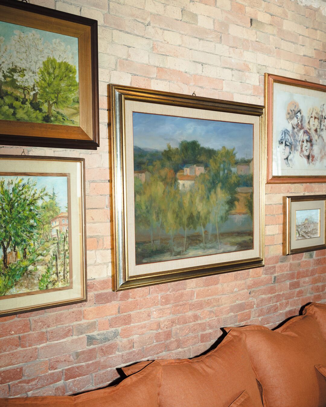 A brick wall with multiple framed paintings.