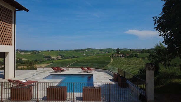 Un área de piscina con sillones reclinables, vistas despejadas a viñedos y un edificio con fachada de celosía.