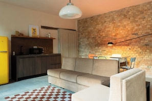 Un espace de vie compact comprenant un canapé, une table à manger avec des chaises, un coin cuisine avec un réfrigérateur et un mur en briques.